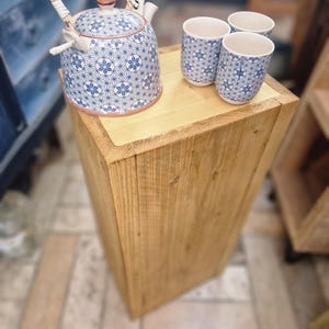 Op de afbeelding: Een blauw-wit bloemmotief keramische theepot met een geweven handvat en drie bijpassende kopjes. De theeset wordt gepresenteerd op een lichtgekleurde houten standaard. De theepot en kopjes hebben een herhalend stervormig ontwerp.