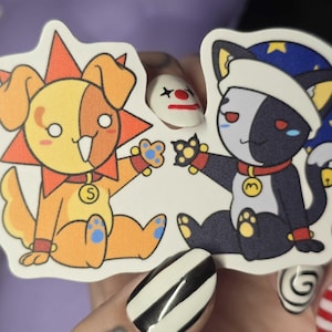 May include: Two cartoon stickers featuring a sun-dog and a moon-cat. The sun-dog is orange and yellow with a red collar. The moon-cat is black and white with a nightcap. Both are giving a high-five.