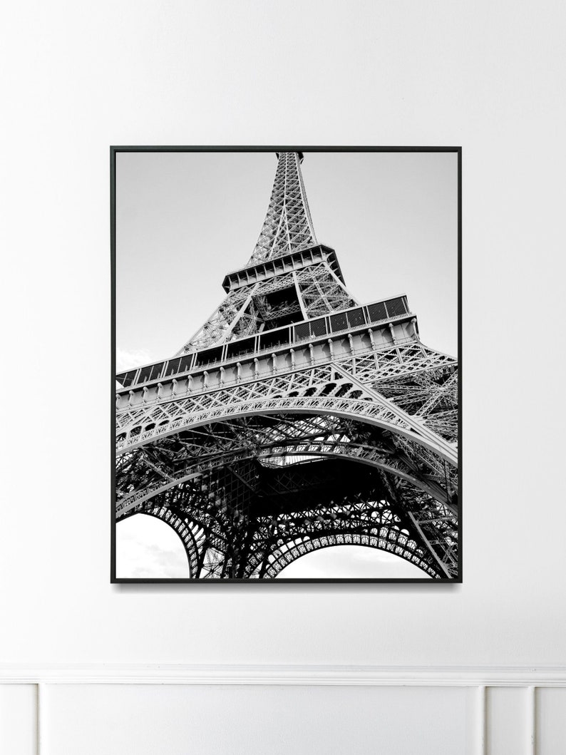 以下が含まれることがあります： フランスのパリにあるエッフェル塔の白黒写真。写真は低い角度から撮影されており、塔を見上げています。塔の複雑な金属構造が見えます。