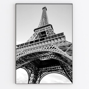 以下が含まれることがあります： フランスのパリにあるエッフェル塔の白黒写真。写真は低い角度から撮影されており、塔を見上げています。塔は金属製で、複雑なデザインをしています。