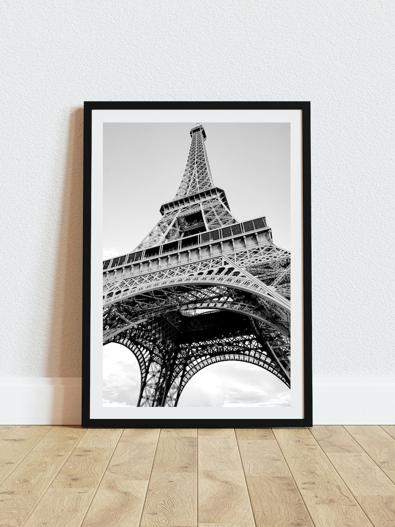 May include: A black and white photograph of the Eiffel Tower in Paris, France. The photo is taken from a low angle, looking up at the tower. The tower is made of metal and has a intricate design. The sky is cloudy.