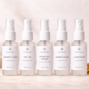 Pode incluir: Cinco frascos de spray de vidro transparente com tampas brancas, rotulados com diferentes aromas: Desert Haze, Mai Tai, Honeyed Amber, Amber Musk e Lavender. Cada frasco tem 28g. Os frascos estão dispostos sobre uma superfície clara.