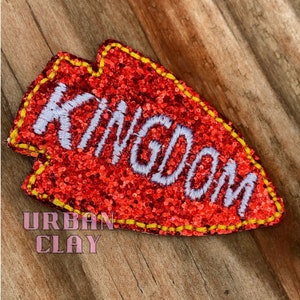 May include: Red glitter arrow with a yellow outline and the word "Kingdom" embroidered in white.