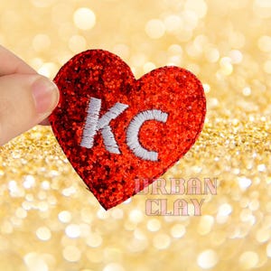 May include: Red glitter heart-shaped patch with white embroidered letters "KC" in the center.