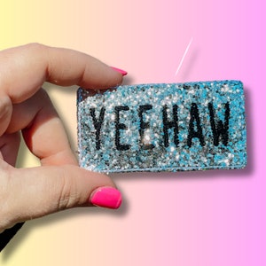 May include: A silver glitter rectangle with the word "Yeehaw" in black lettering.