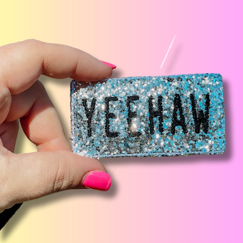 May include: A silver glitter rectangle with the word "Yeehaw" in black lettering.
