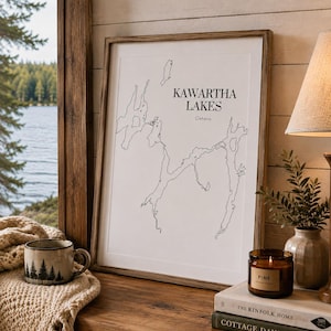 May include: A framed vertical wall art print featuring a black line map of the Kawartha Lakes in Ontario, Canada. The print has a white background with the text Kawartha Lakes and Ontario printed in a black serif font centred at the top.