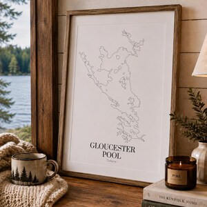 Könnte beinhalten: Ein gerahmter Wandkunstdruck mit einer schwarzen Linienkarte von Gloucester Pool, Ontario, auf weißem Hintergrund. Der Text Gloucester Pool Ontario ist unten auf der Karte in Schwarz gedruckt. Der Rahmen besteht aus mittelbraunem Holz.