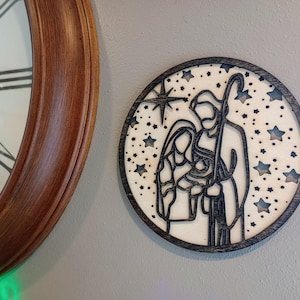 May include: A wooden Christmas ornament featuring a silhouette of the Holy Family with a star and a night sky background.