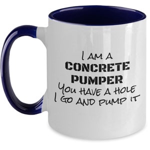 May include: White ceramic coffee mug with a blue rim. The mug has black text that reads "I am a Concrete Pumper You have a hole I go and pump it."