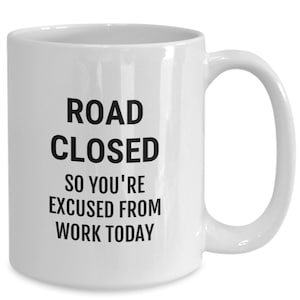 May include: White ceramic coffee mug with black text that reads "ROAD CLOSED SO YOU'RE EXCUSED FROM WORK TODAY".
