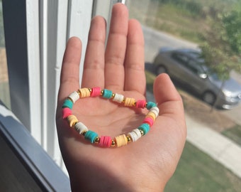 May include: A colorful beaded bracelet with white, pink, yellow, and turquoise beads. The beads are stacked and have a gold accent.