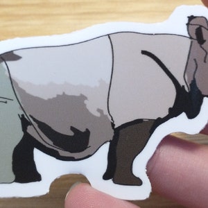 Puede incluir: Una pegatina de rinoceronte gris y marrón con un contorno blanco. El rinoceronte está mirando hacia el lado derecho de la imagen.