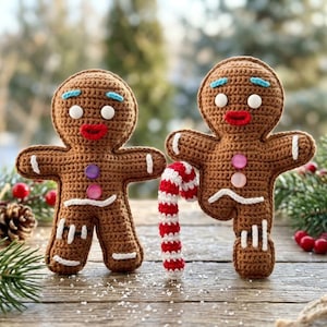 May include: Two brown crocheted gingerbread figures with white stitched details, red lips, blue eyebrows, and round white eyes. The figures feature colorful buttons on their chests and one holds a red and white striped crocheted candy cane.