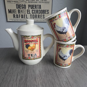May include: A white ceramic tea set featuring a teapot and two mugs. The teapot and mugs have a rooster design with the word "ROOSTER" and "TEA" printed on them. The background includes a vintage poster.