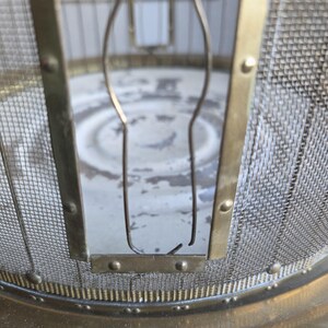 May include: Close-up of a vintage brass and mesh fire screen. The screen features a fine metal mesh, a brass frame, and decorative details. The design suggests a focus on safety and aesthetic appeal for a fireplace.
