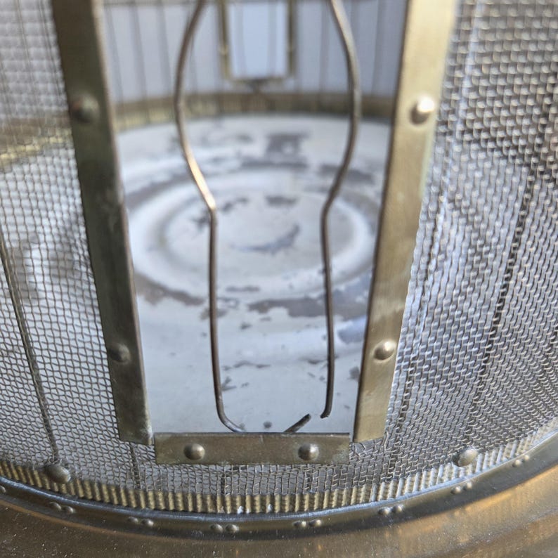 May include: Close-up of a vintage brass and mesh fire screen. The screen features a fine metal mesh, a brass frame, and decorative details. The design suggests a focus on safety and aesthetic appeal for a fireplace.