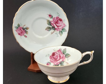May include: White teacup and saucer set with pink rose floral design and gold trim. The teacup has a handle and sits on a pedestal base. The saucer has a scalloped edge.