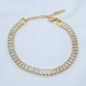 May include: A gold bracelet with a chain and a row of clear rectangular stones.