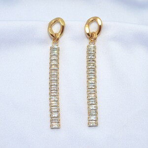 May include: Gold dangle earrings with a long chain of clear rectangular crystals.