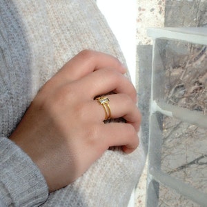 May include: A gold ring with a clear rectangular stone set in a double band.