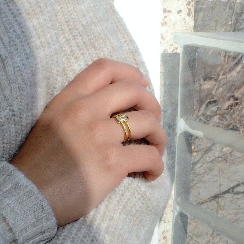 May include: A gold ring with a clear rectangular stone set in a double band.