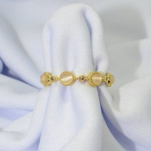 May include: A gold ring with four white oval stones and small clear stones between each stone.