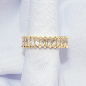 May include: A gold band ring with a row of clear baguette-shaped cubic zirconia stones.