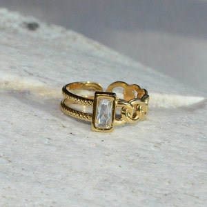 May include: A gold ring with a chain design and a clear rectangular stone.