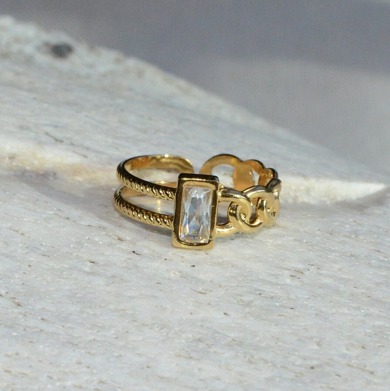 May include: A gold ring with a chain design and a clear rectangular stone.