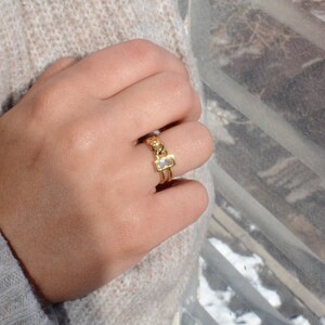 May include: Gold ring with a rectangular clear stone set in a chain link design.