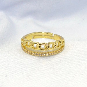 May include: A gold ring with a double band design. The top band is a thick chain link style and the bottom band is a thin band of small clear stones.