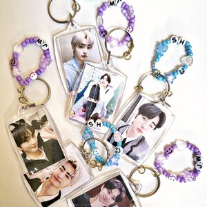 May include: Six keychains with clear photo frames featuring different photos of a young man. Each keychain has a beaded charm with the letters "SH", "MC", or "JW" in white.