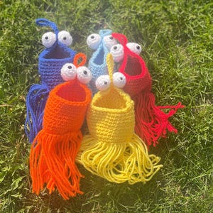 Könnte beinhalten: Fünf gehäkelte Hängekörbe mit Glitzern und Fransen. Die Körbe sind in Blau, Rot, Gelb und Orange.