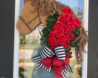 May include: A brown horse head wreath with a red rose bouquet and a black and white striped bow.
