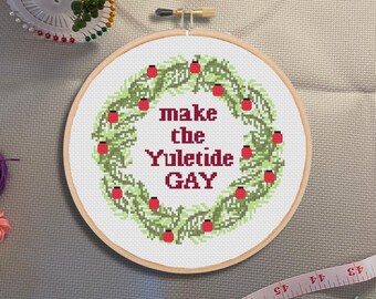 May include: An embroidered wreath in green and red with the text "make the Yuletide GAY" in red.