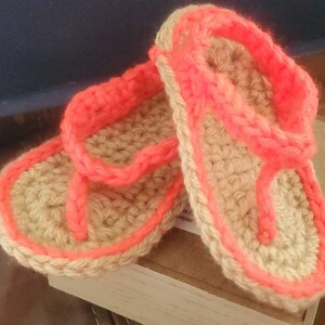 May include: A pair of crocheted flip-flops with a tan base and bright pink trim. The flip-flops are made with a simple crochet stitch and have a comfortable, casual look.