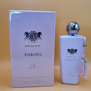 May include: A pink and white bottle of Dakota Parfum d'Elite perfume with a silver cap and a pink tassel. The bottle is sitting on a white box with the same design.