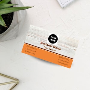 May include: A business card with a wood grain background and a brown and orange color scheme. The card has a black circle with the text "YOUR LOGO" in white. The text "Business Name" and "Your Name" is in black. The card has three lines of contact information.