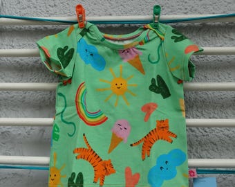 May include: A green short-sleeved t-shirt with a colourful print of suns, rainbows, ice cream cones, clouds, cacti, and tigers.