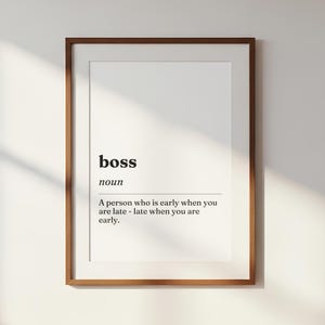 Op de afbeelding: Een ingelijste wandkunstprint met een woordenboekdefinitie van het woord boss. De tekst luidt: boss, noun, A person who is early when you are late - late when you are early. De print zit in een eenvoudige bruine houten lijst.