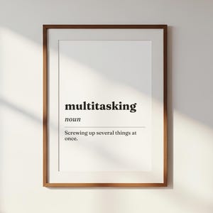 Può includere: Una stampa artistica da parete incorniciata che presenta una definizione da dizionario della parola multitasking. Il testo recita multitasking, noun, Screwing up several things at once. La stampa è inserita in una cornice di legno marrone.