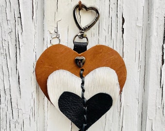 May include: A brown leather heart-shaped keychain with a white and black cowhide heart layered on top. The keychain has a black tassel with white and black beads and a turquoise bead.