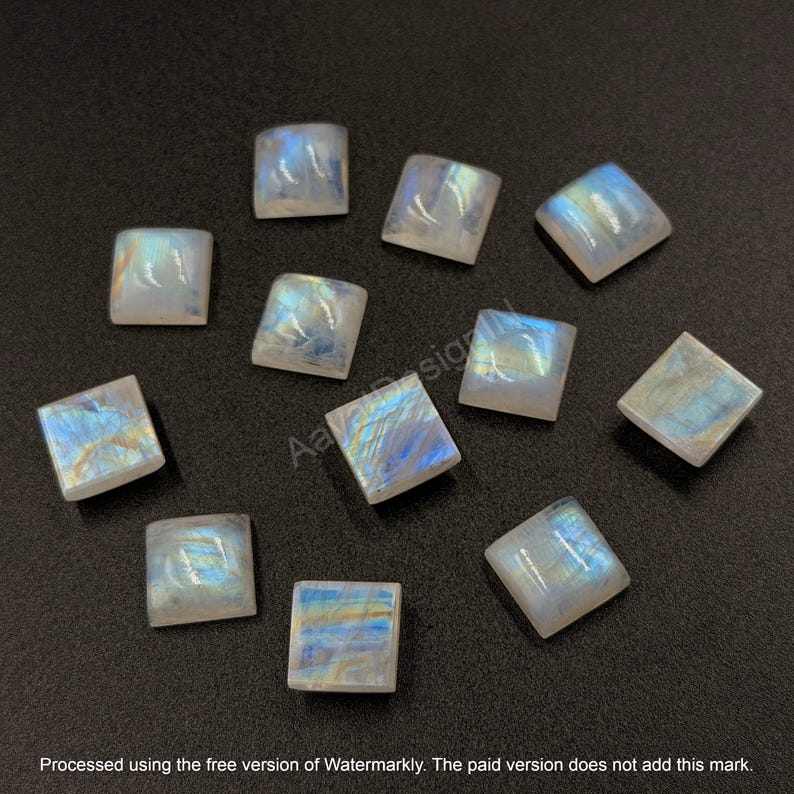 May include: A collection of eleven square-shaped moonstone cabochons with a smooth, polished surface. Each stone displays a translucent, milky white appearance with iridescent blue and gold flashes that shift in the light.