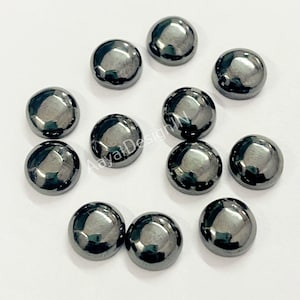 May include: A collection of twelve round, black, glass cabochons. The cabochons are smooth and shiny.