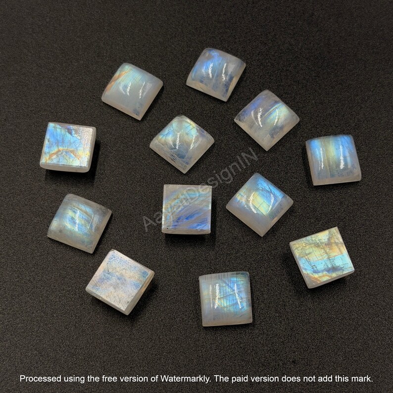 May include: A collection of eleven square-cut moonstone cabochons featuring a translucent white base with iridescent blue and gold flashes. Each gemstone displays a smooth, polished surface with a distinct adularescence effect.