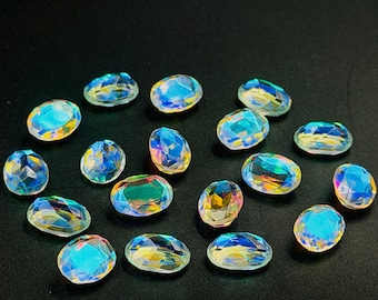 May include: A collection of iridescent, oval-shaped gemstones. The gems display a spectrum of colors, including blues, greens, and yellows, with a faceted surface that catches the light. The stones are scattered on a dark background.