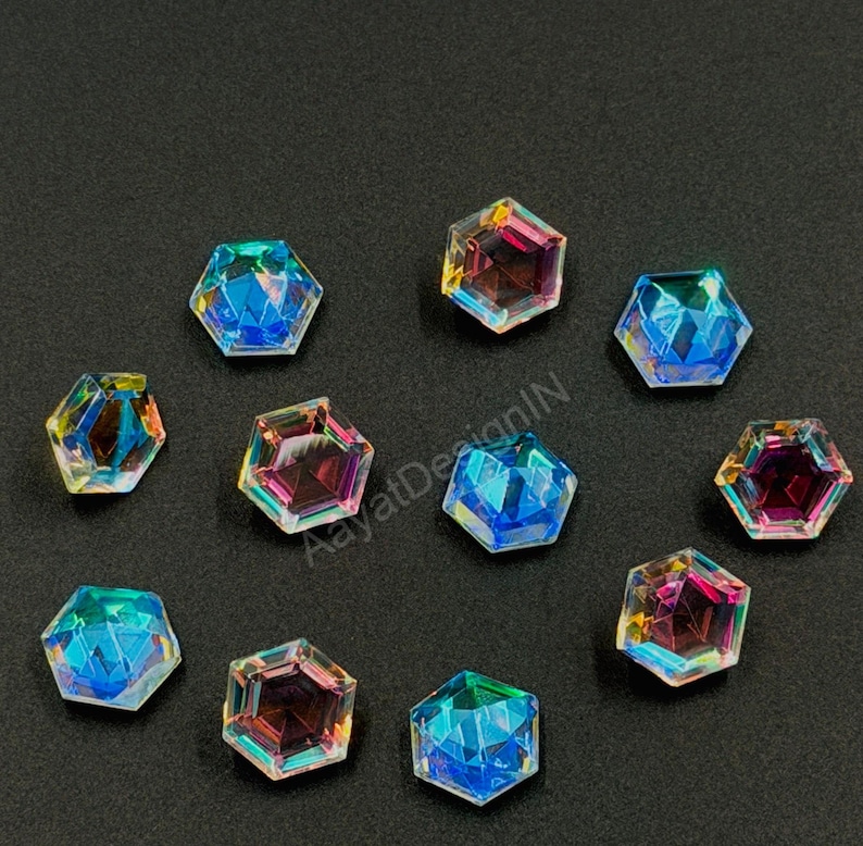 May include: A collection of iridescent, hexagonal crystals. The crystals display a spectrum of colors, including blues, pinks, and yellows, with a faceted design. They are scattered on a dark surface, creating a sparkling effect.
