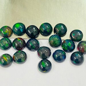 May include: A collection of 15 round black opal cabochons with green, red, and orange iridescent flashes. The cabochons are approximately 6mm in diameter.