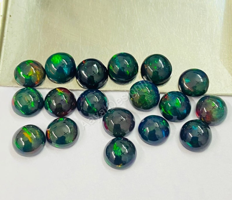 May include: A collection of 15 round black opal cabochons with green, red, and orange iridescent flashes. The cabochons are approximately 6mm in diameter.